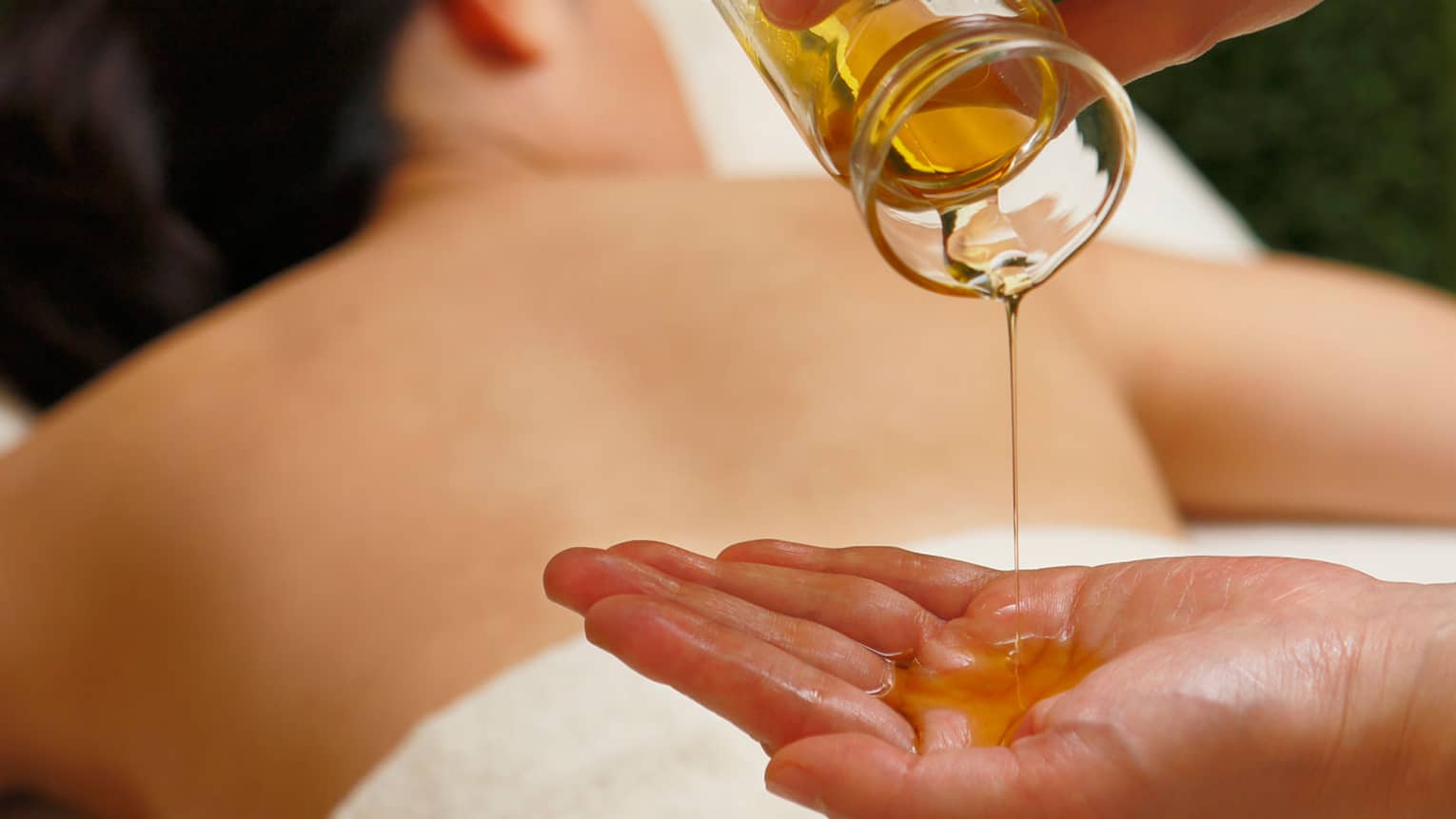 Spa staff pours massage oil into hand over woman's back