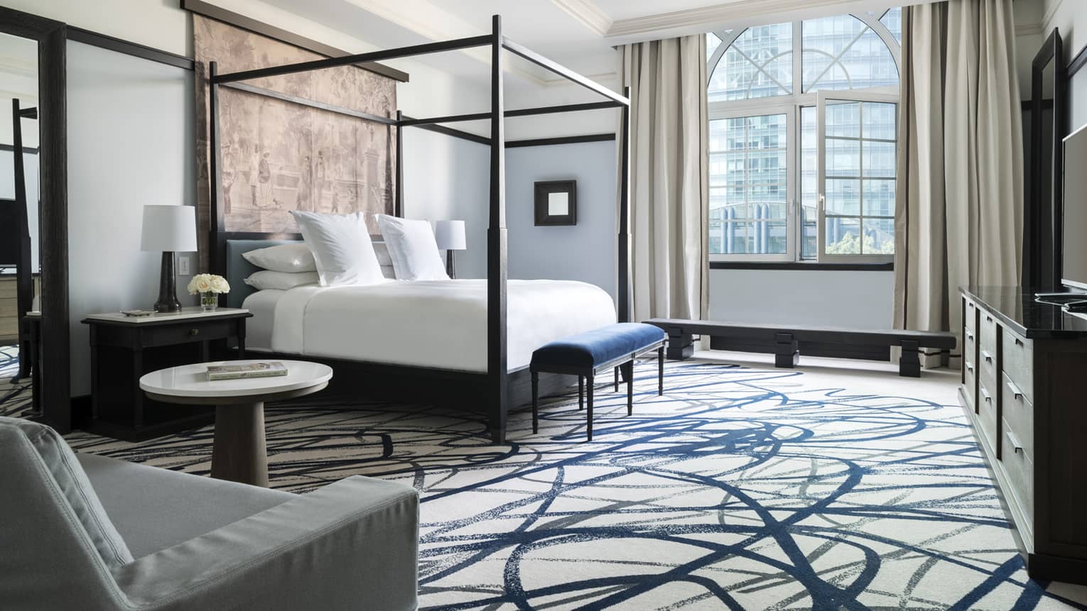 Hotel room with poster bed by arched window, carpeted floor with swirl pattern