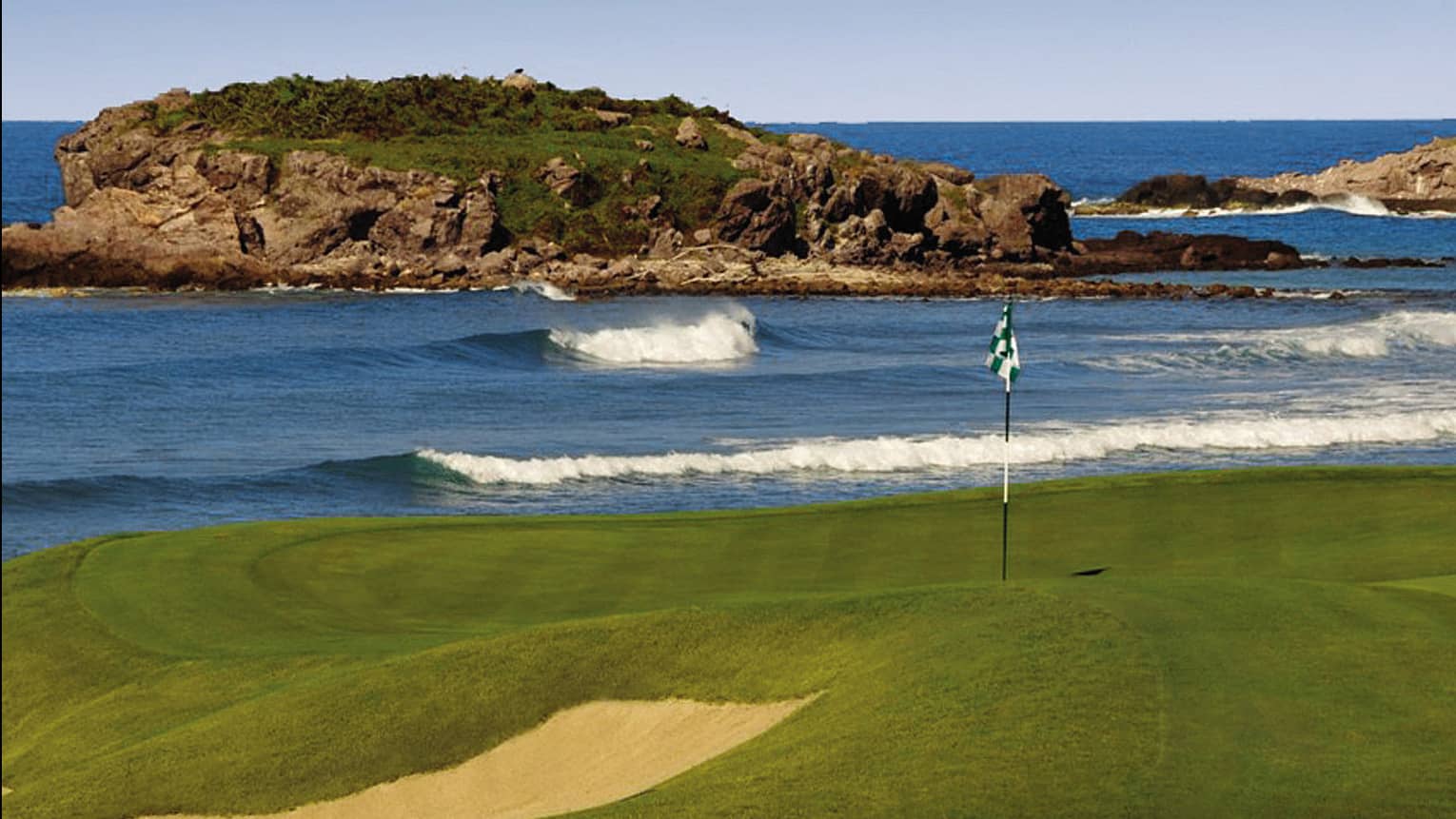 Bahia Golf Course flag on green beside rolling ocean tide, large rock