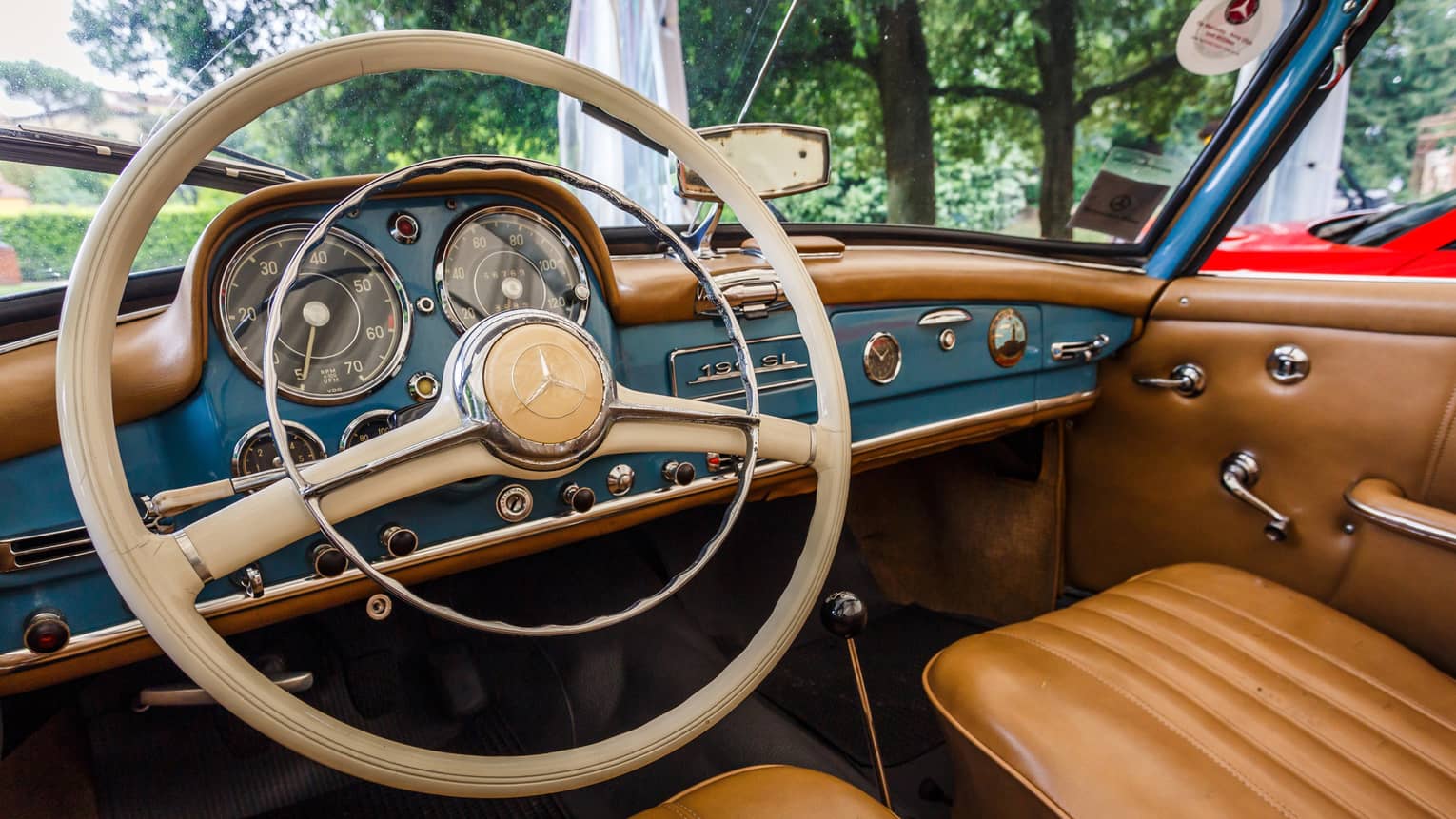 Close-up of vintage car steering wheel, dashboard and dials, tan leather seats