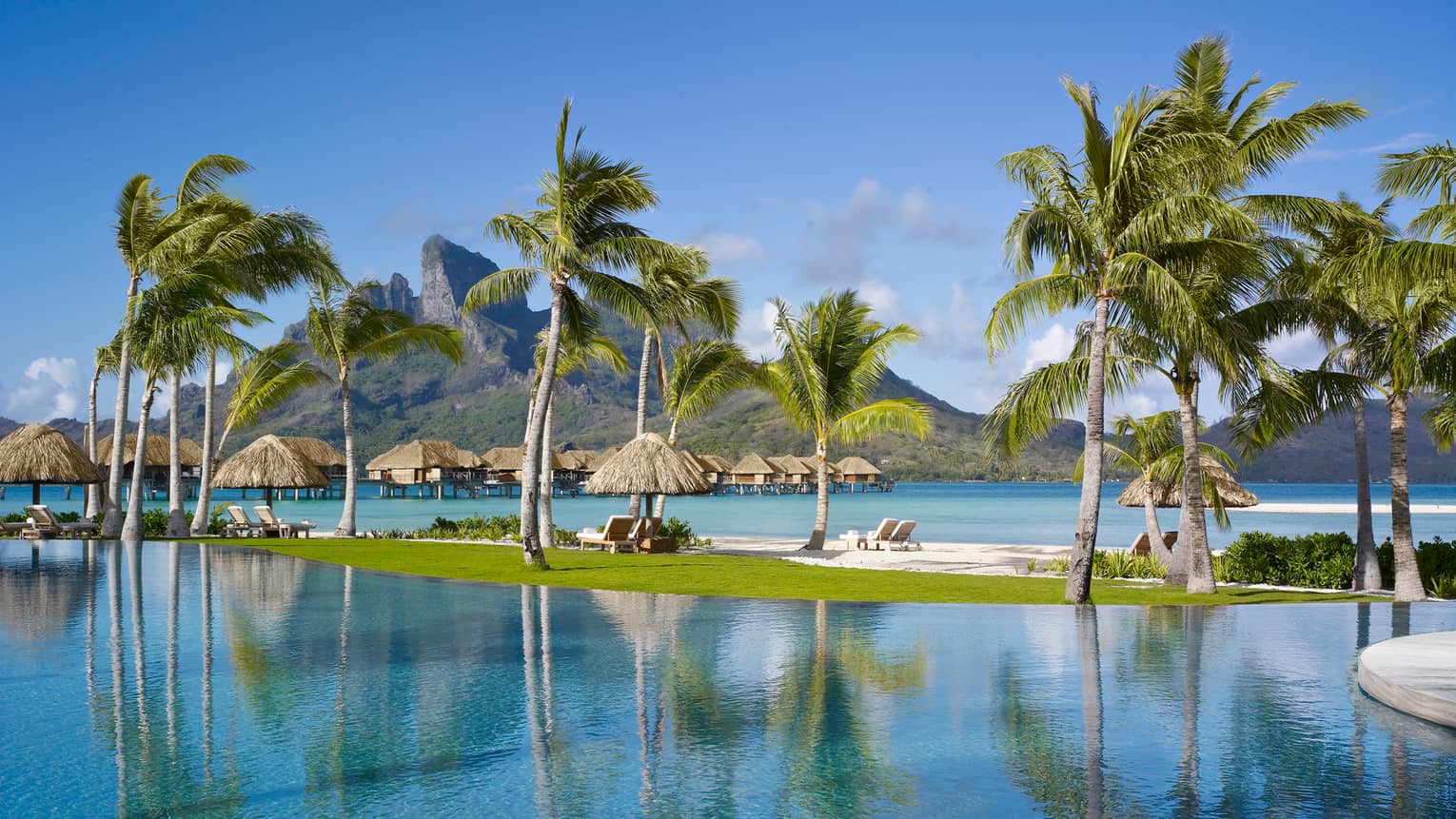 Patio lounge chairs, tall palm trees on sandbar in lagoon