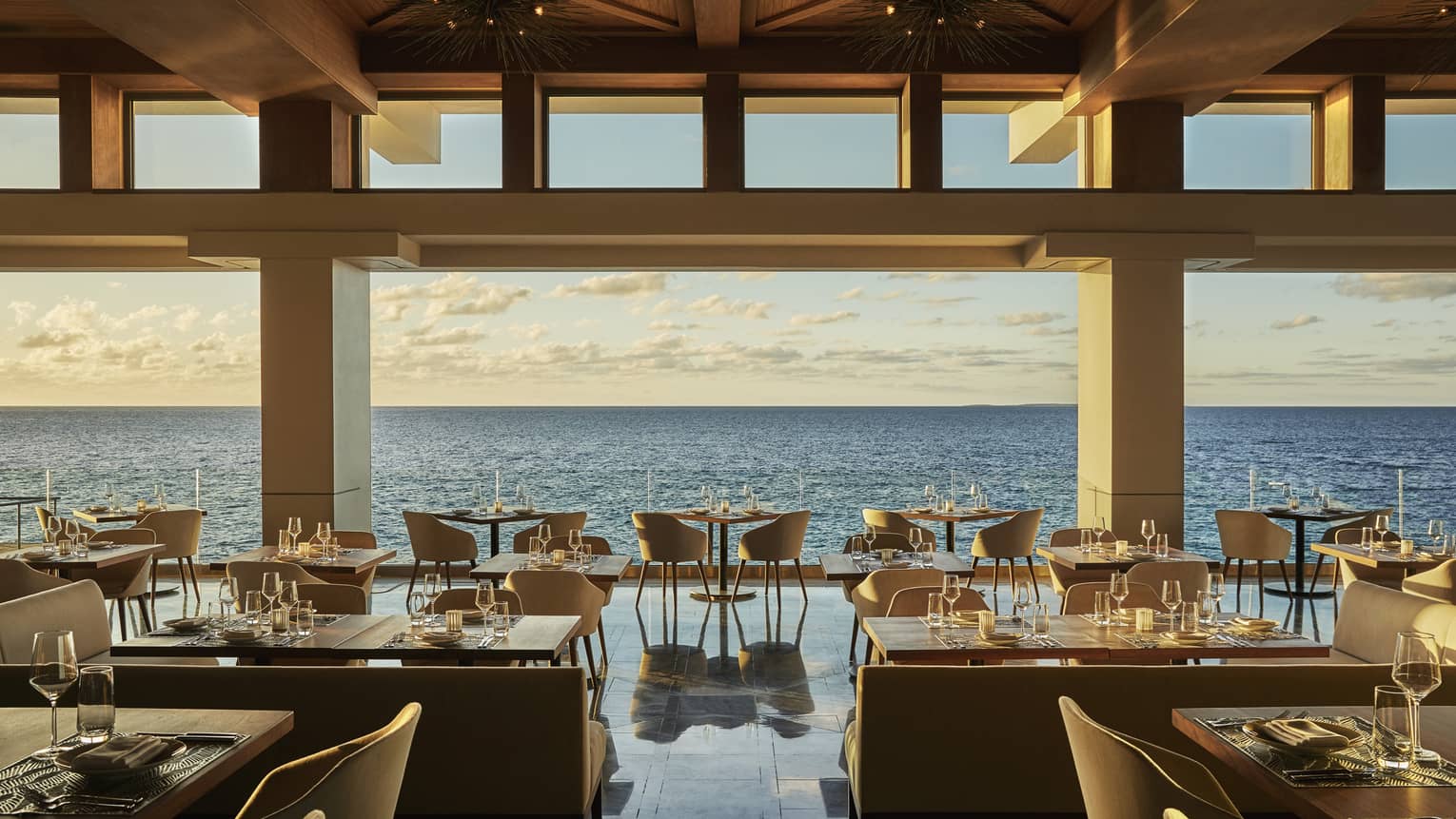 Dining tables, chairs for two in row along outdoor bar overlooking ocean