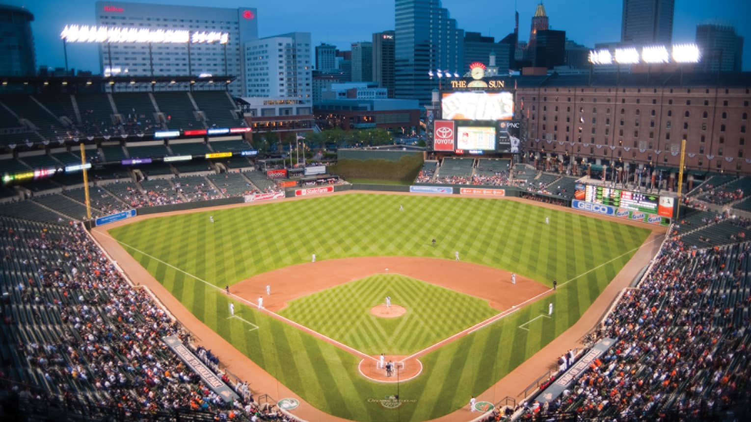 View over large open air baseball stadium with crowds in stands, city buildings in background