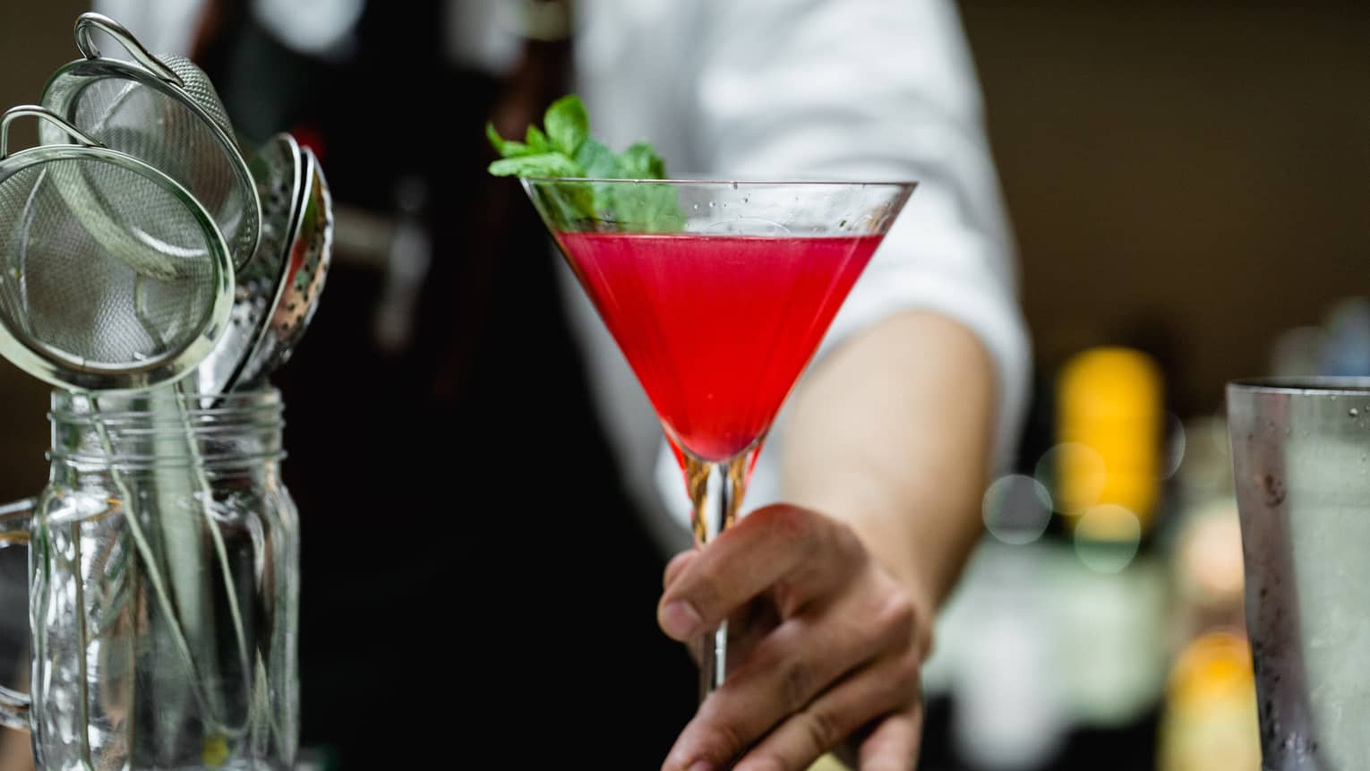 Close-up of bartender holding red cocktail in martini glass on bar
