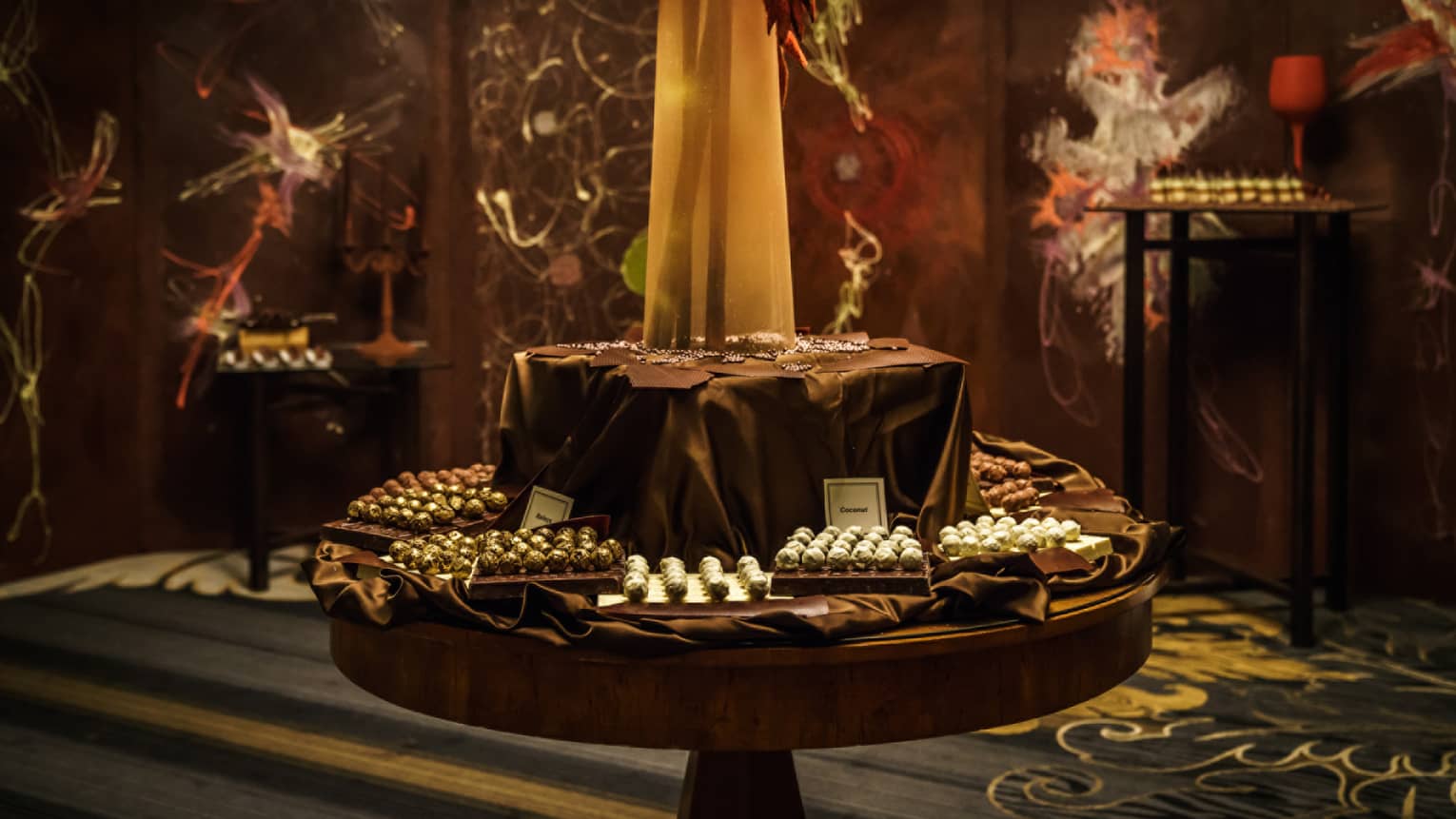 Two-tiered display table with dark brown silk cloth, boxes of fine chocolates wrapped in gold foil