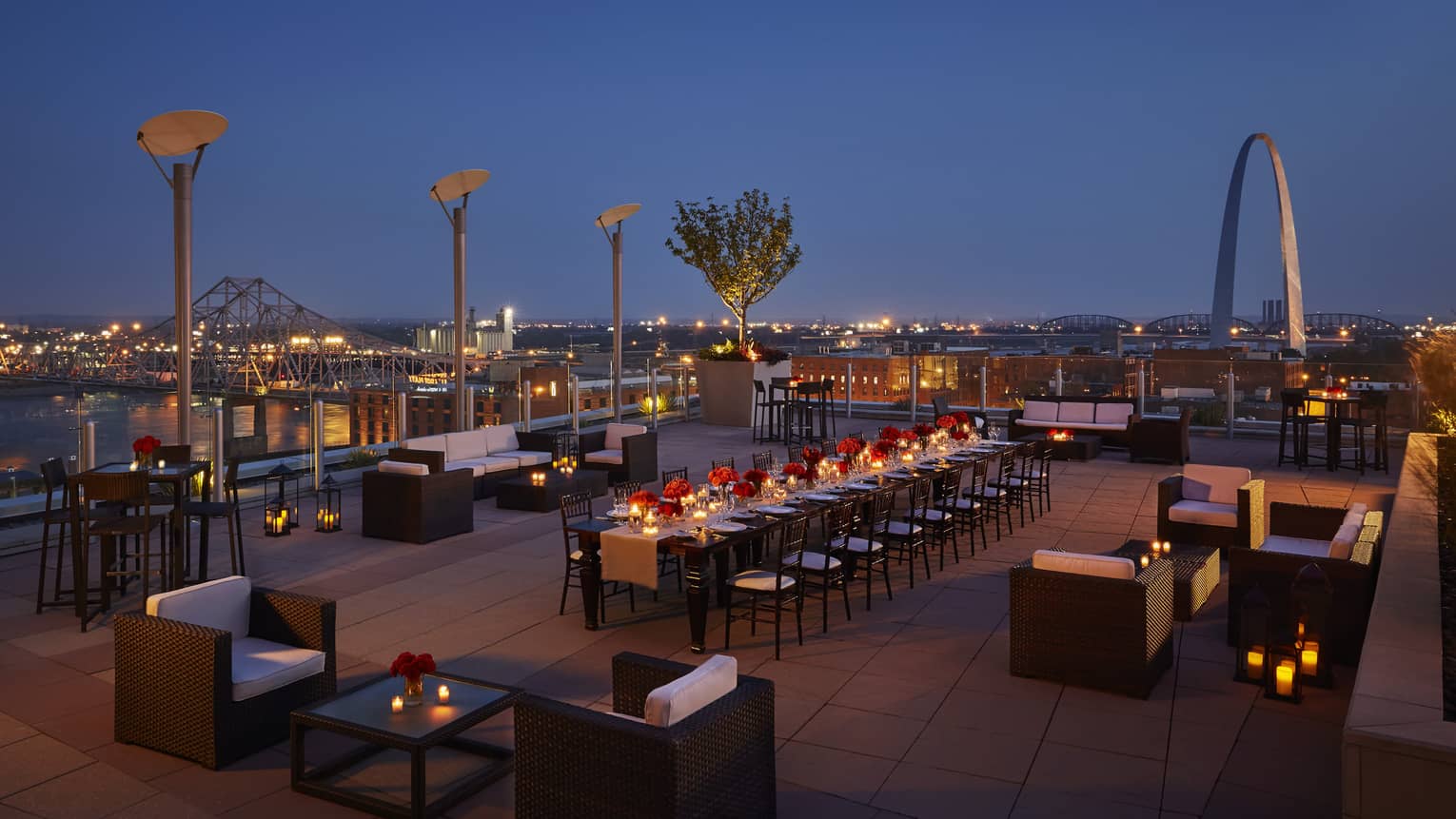 Aerial view of rooftop patio at night with lounge chairs and long communal dining table with candles