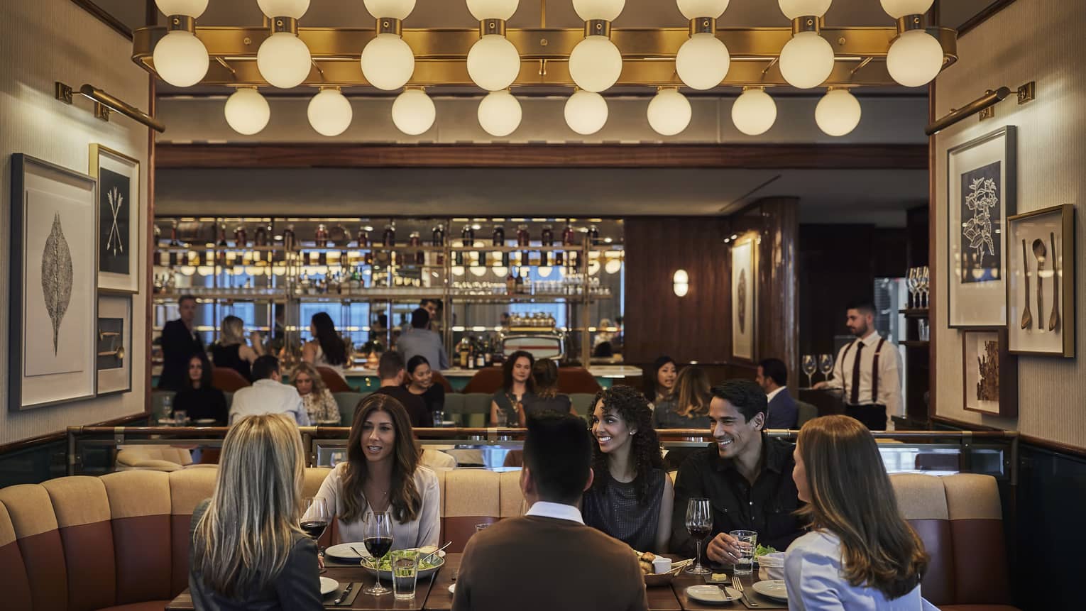 D Bar, groups of friends enjoy cocktails at lounge tables under row of retro bulb lights 