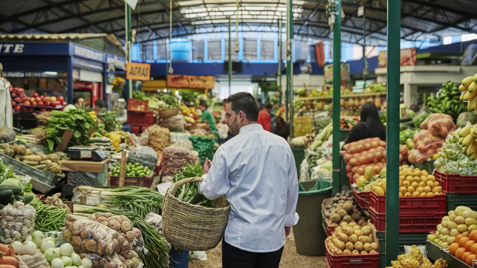 Chef holding large basket walks down aisle of large fruit market