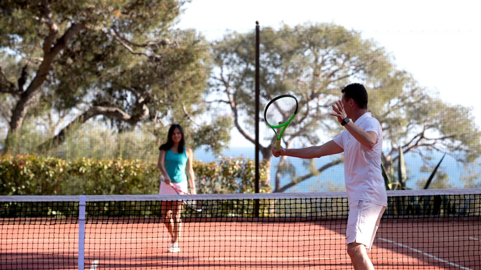 Man swings tennis racket, woman on other side of net