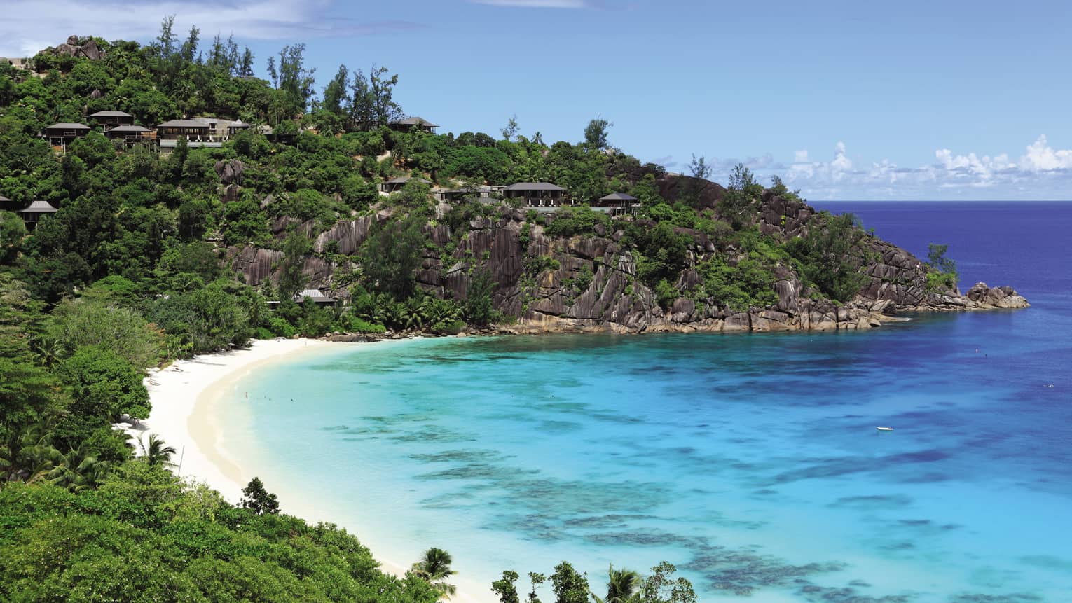 View over bay with lush mountains over white sand beach and turquoise lagoon