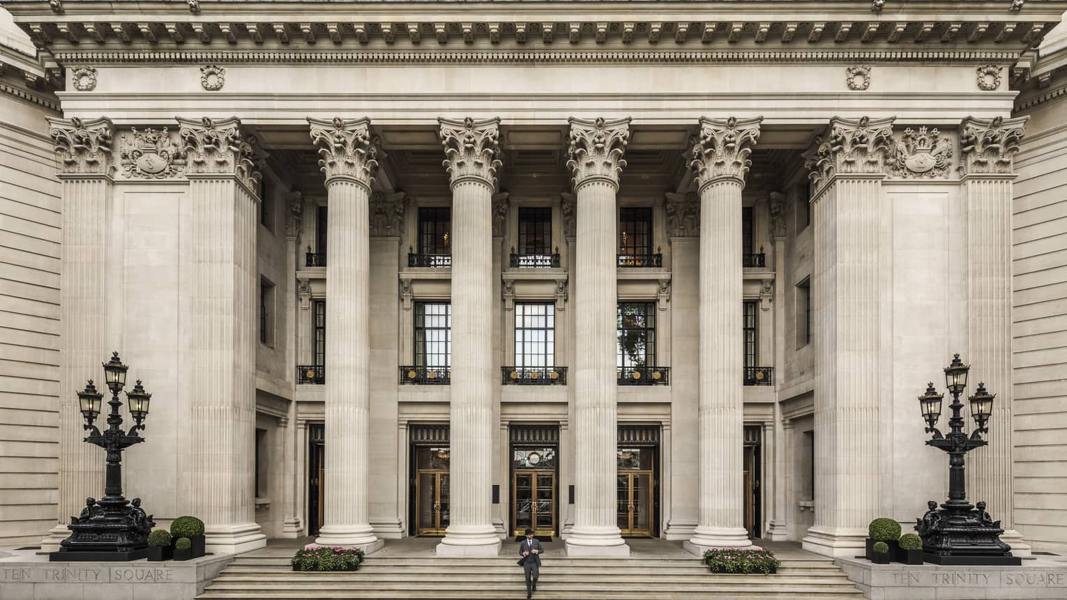 Man in suit and black hat walks down steps under tall white pillars of building
