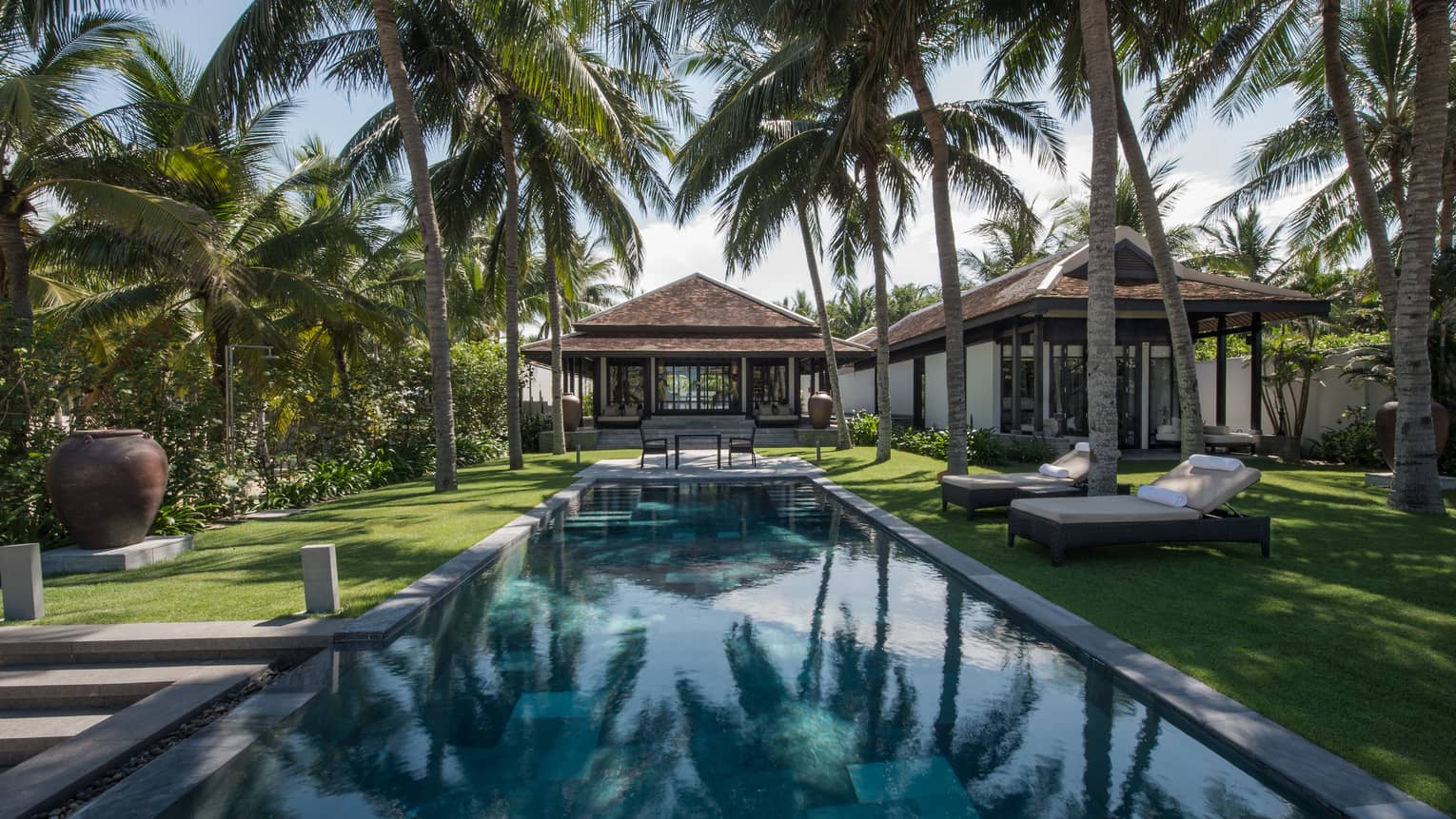 Palm trees reflected on long swimming pool leading to villas