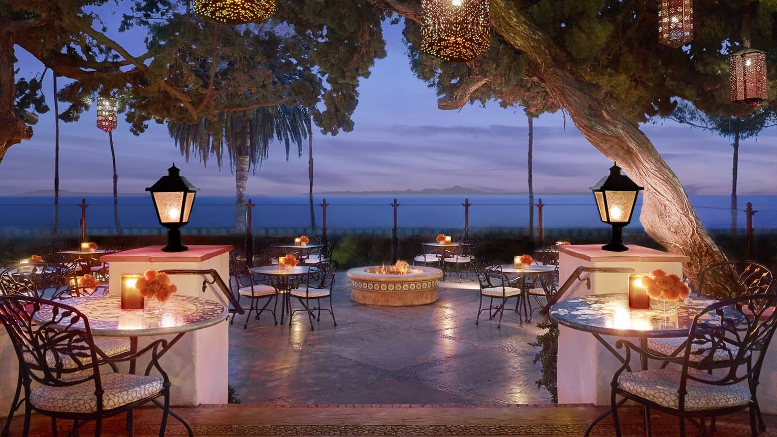 Bella Vista patio at dusk with candle-lit tables under lanterns on posts, hanging from trees