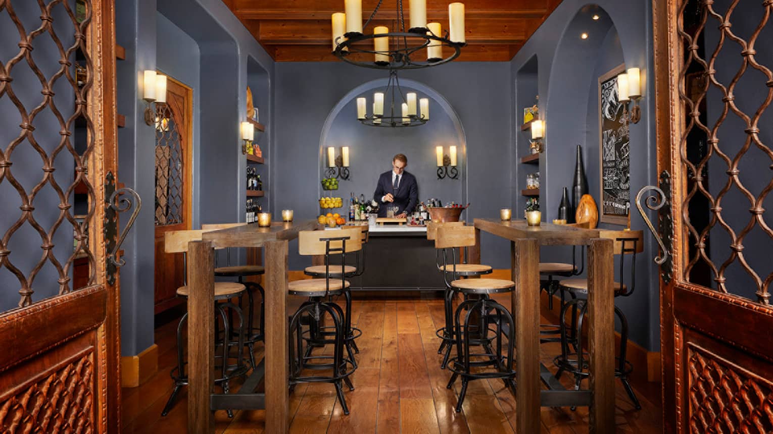 Talavera bartender under arched wall, chandeliers with tall candles behind wood bar tables