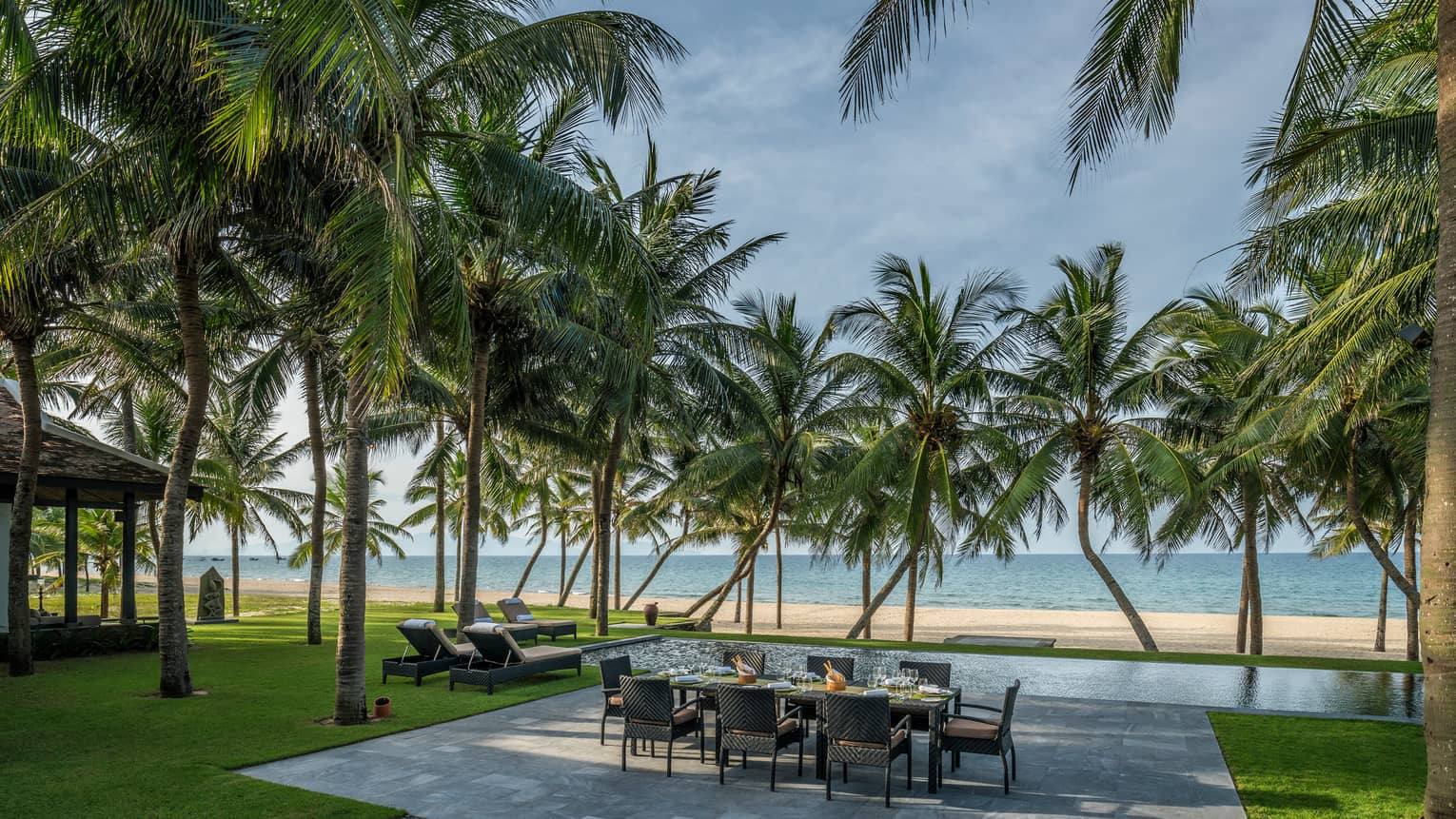 Beachfront Villa large stone patio with private dining table, lounge chairs under palms