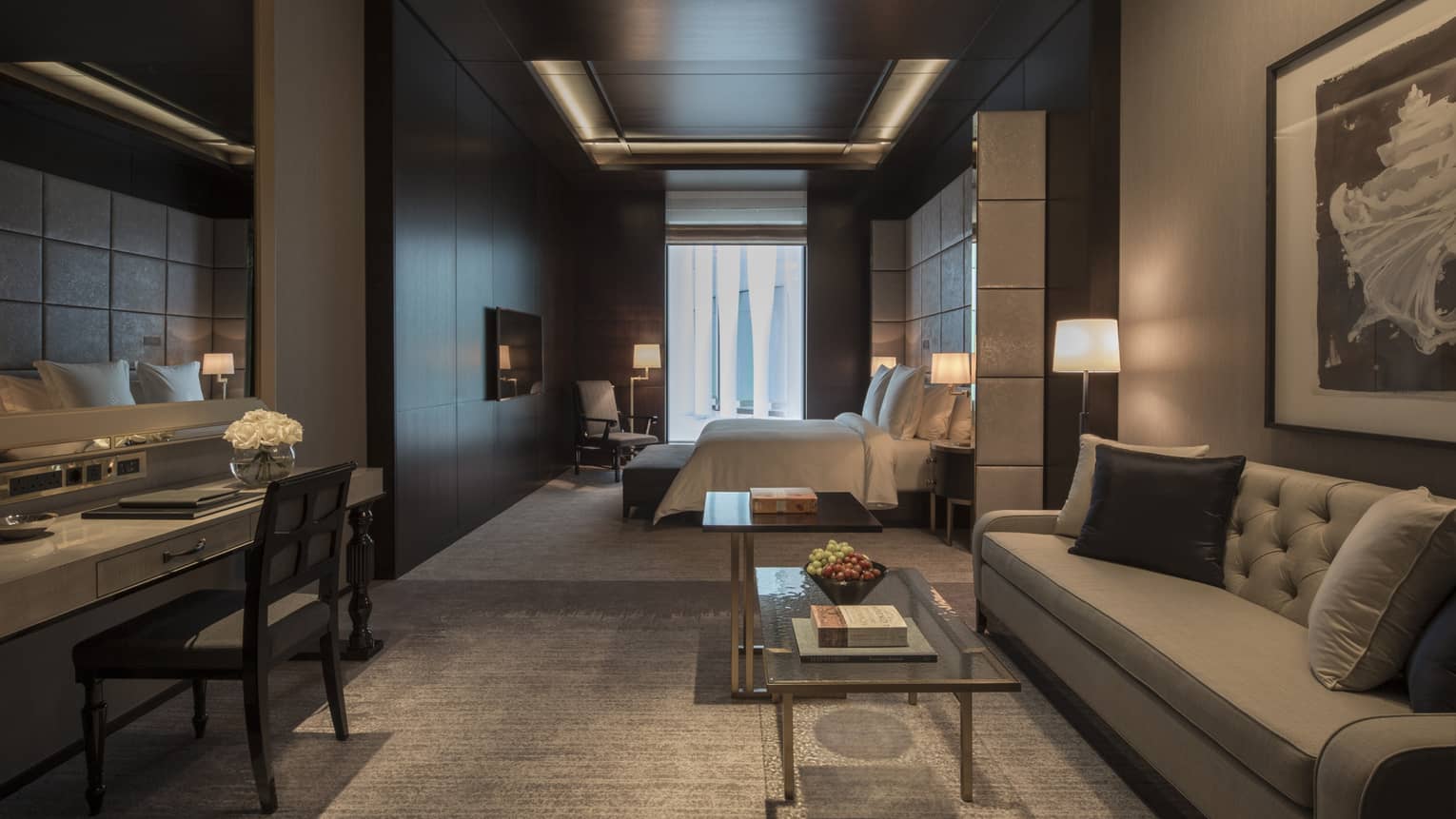 Executive room living area with full-size grey sofa and desk, bedroom in background