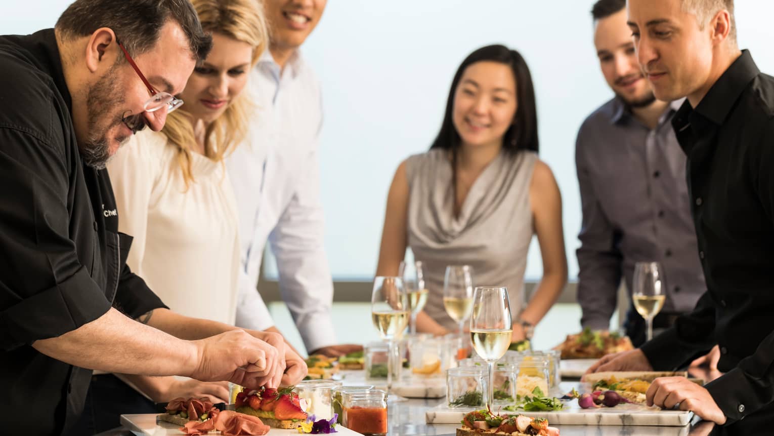 Group of friends watch as chef assembles charcuterie platter, sandwich during cooking class 
