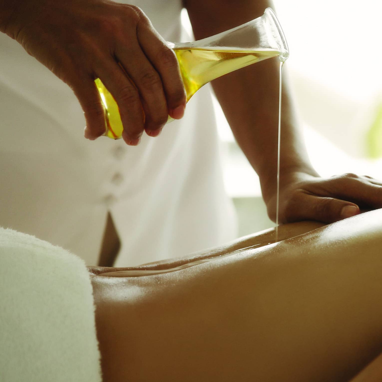 Masseuse pours vile of massage oil over woman's back