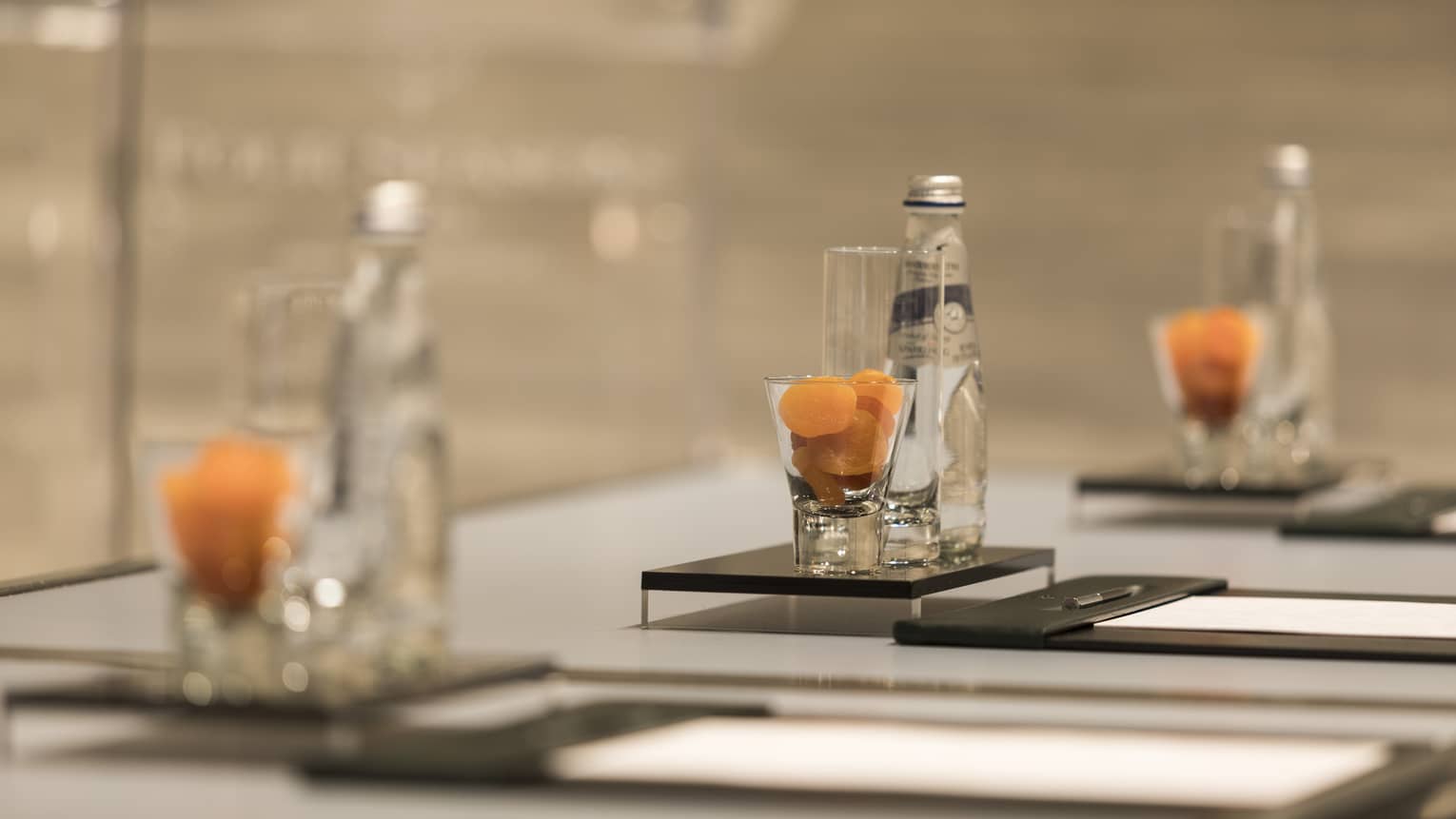 Close-up of meeting table place setting with agenda, dried apricots in glass, bottle of sparkling water
