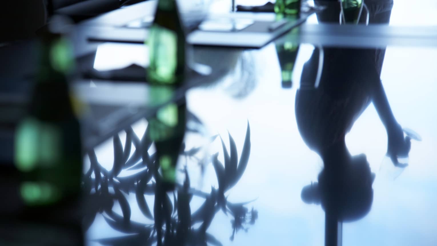 Silhouette of woman reflected on black boardroom table with green bottles