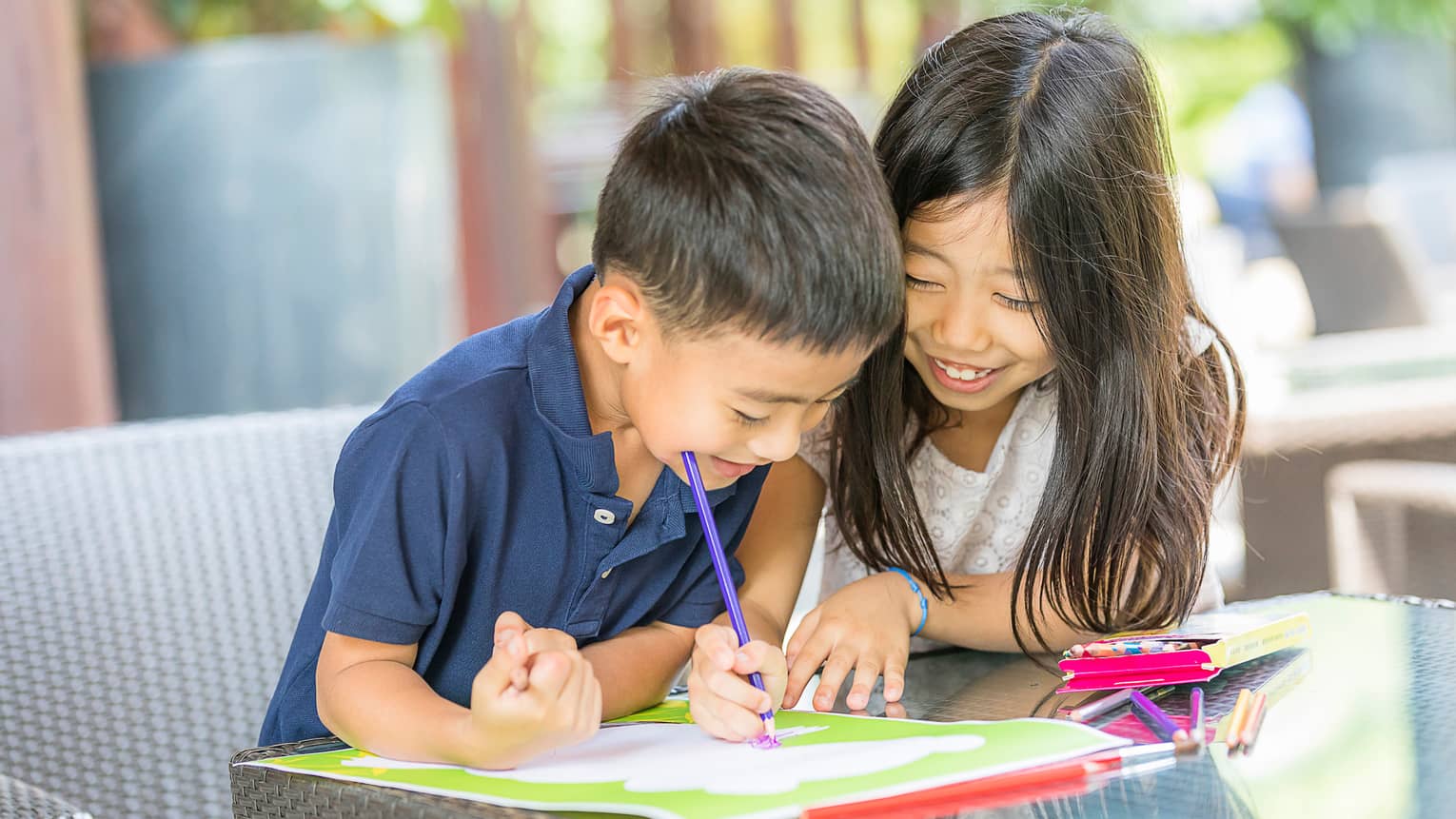 Smiling young boy and girl colouring in book with crayon