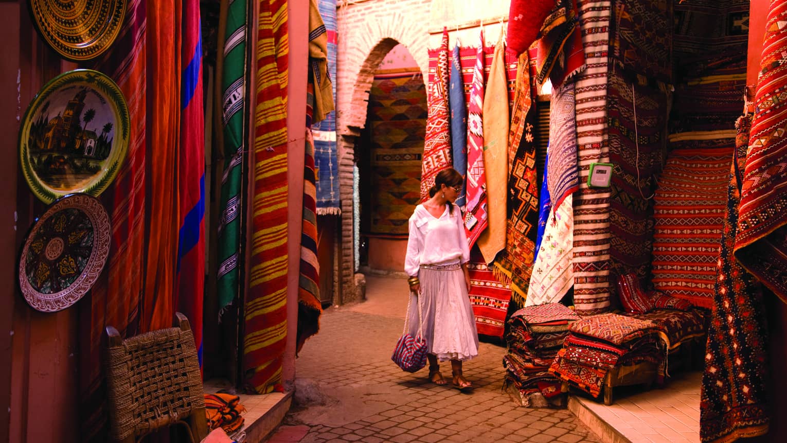 Woman wearing flowing white linen skirt, shirt shops for colourful textiles in market