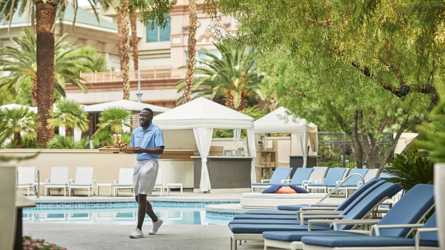 Hotel staff carries tray with Champagne glasses, fruit across Pool Bar patio