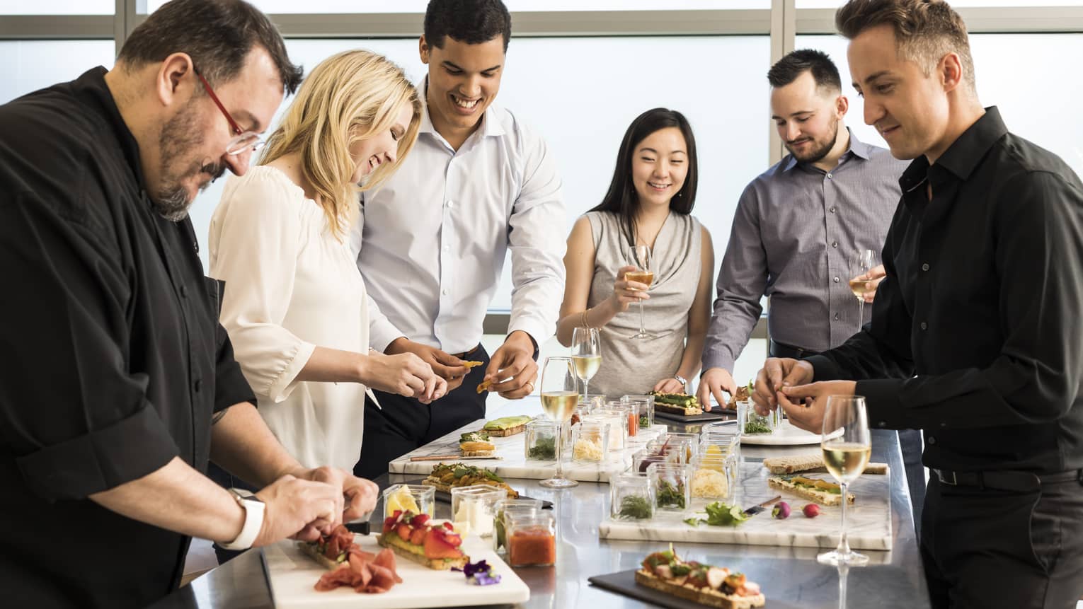 Cooking class, chef and smiling group of guests assemble appetizers at table