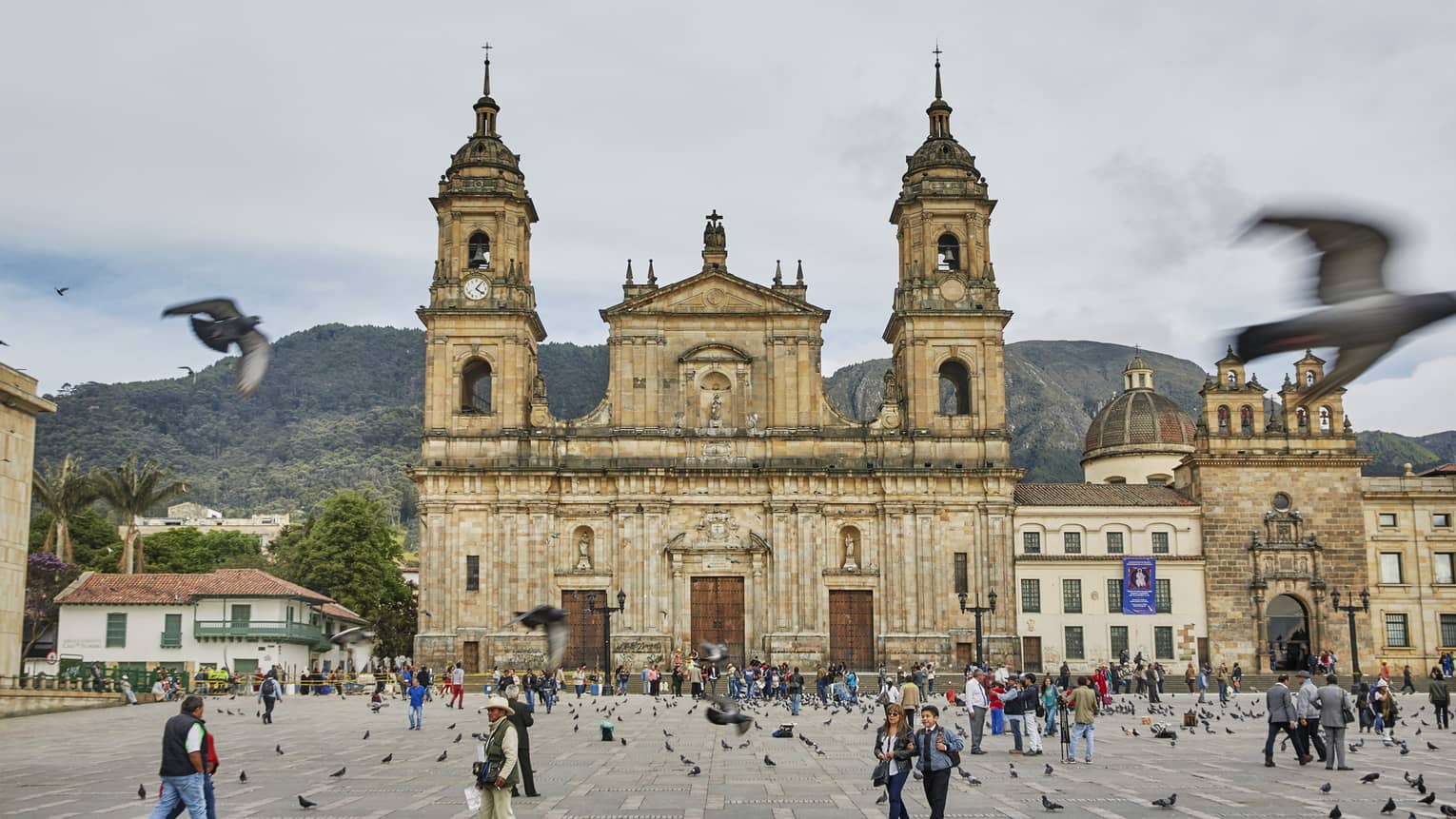 Pigeons fly over crowds in courtyard in front of historic Bogota cathedral