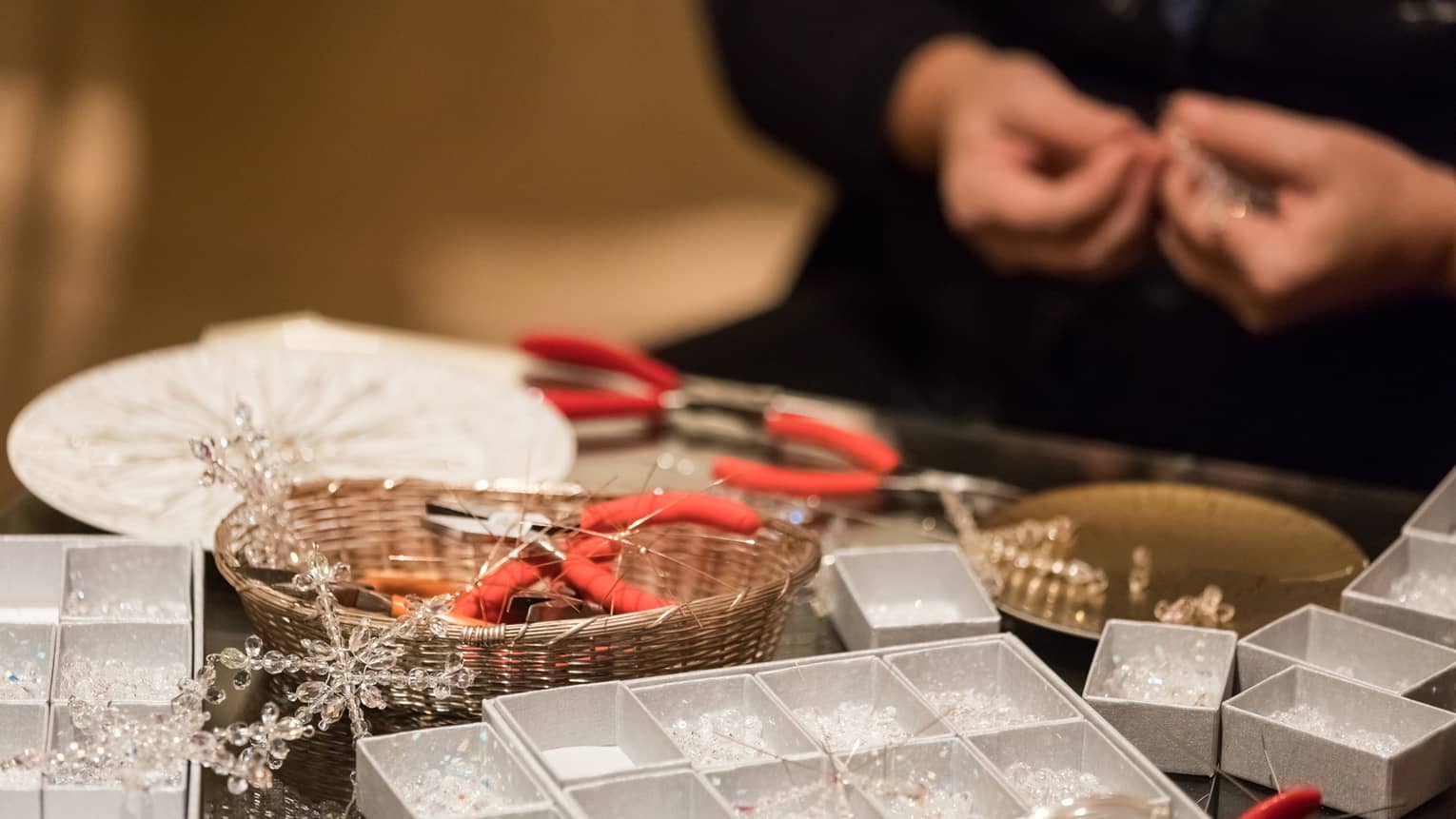 Hands stringing beads behind small craft boxes, jewellery making tools