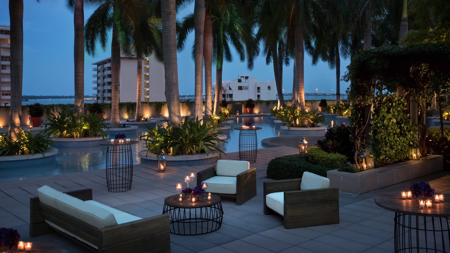 Plush white patio sofas and chairs, candle-lit tables under palm trees at night