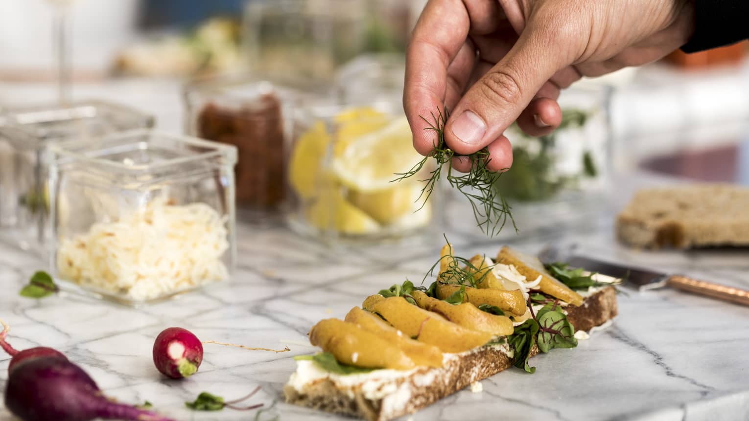 Hand sprinkling fresh herbs on open-faced sandwich on counter
