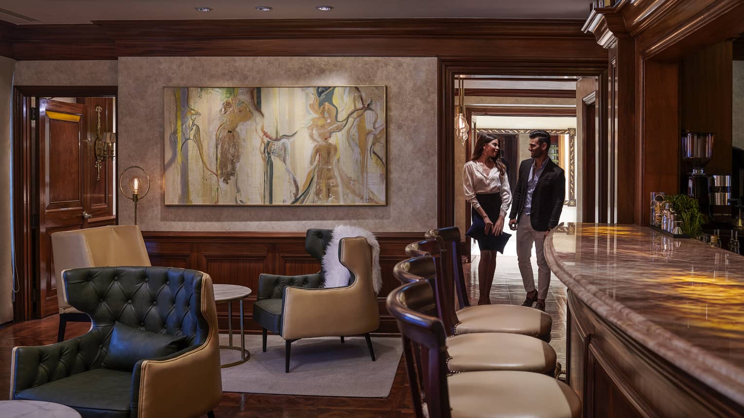 Woman and man walk through door into cocktail lounge with large painting, leather chairs