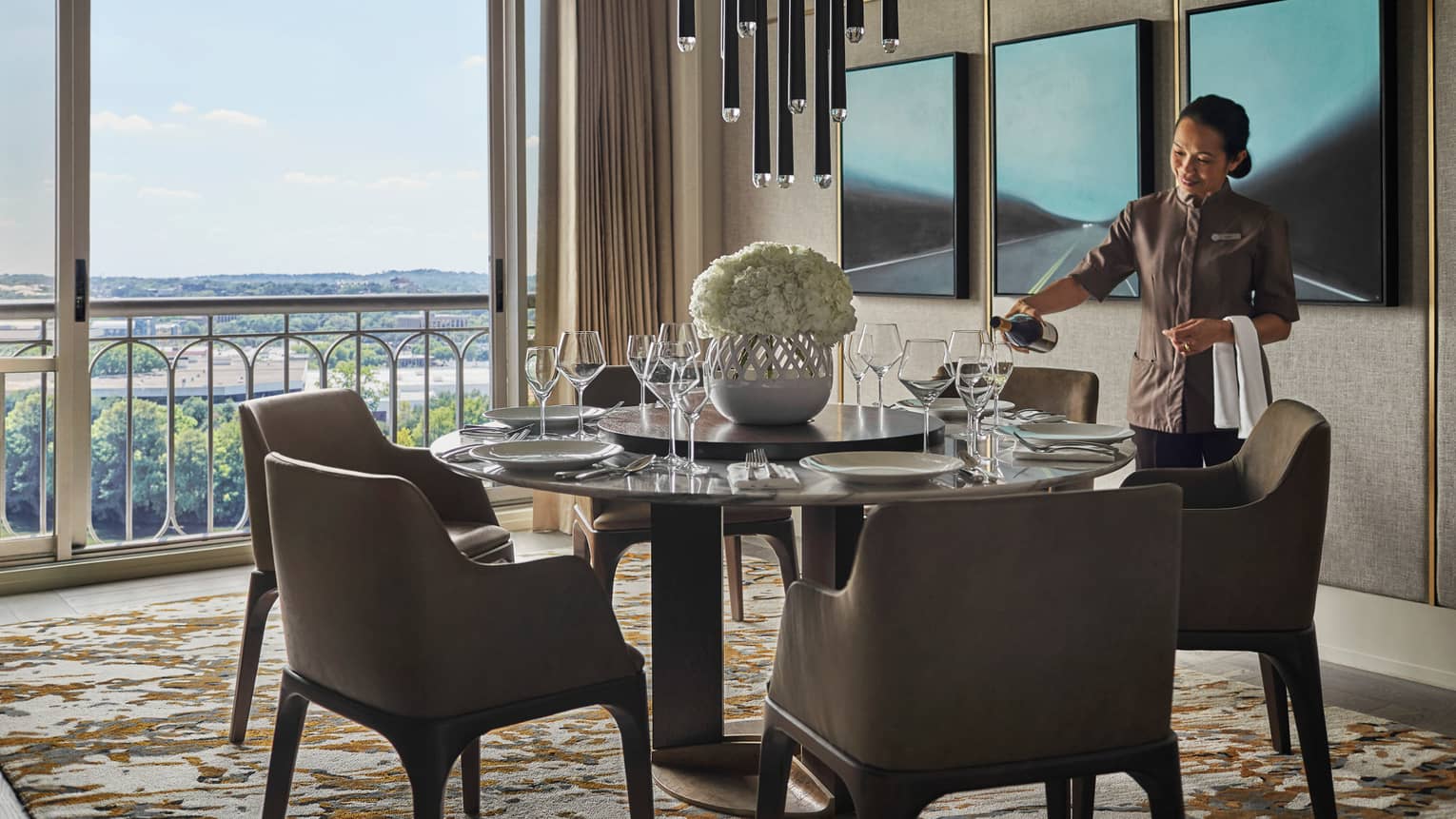 Hotel staff pours wine into glasses at small round table with chairs by sunny window