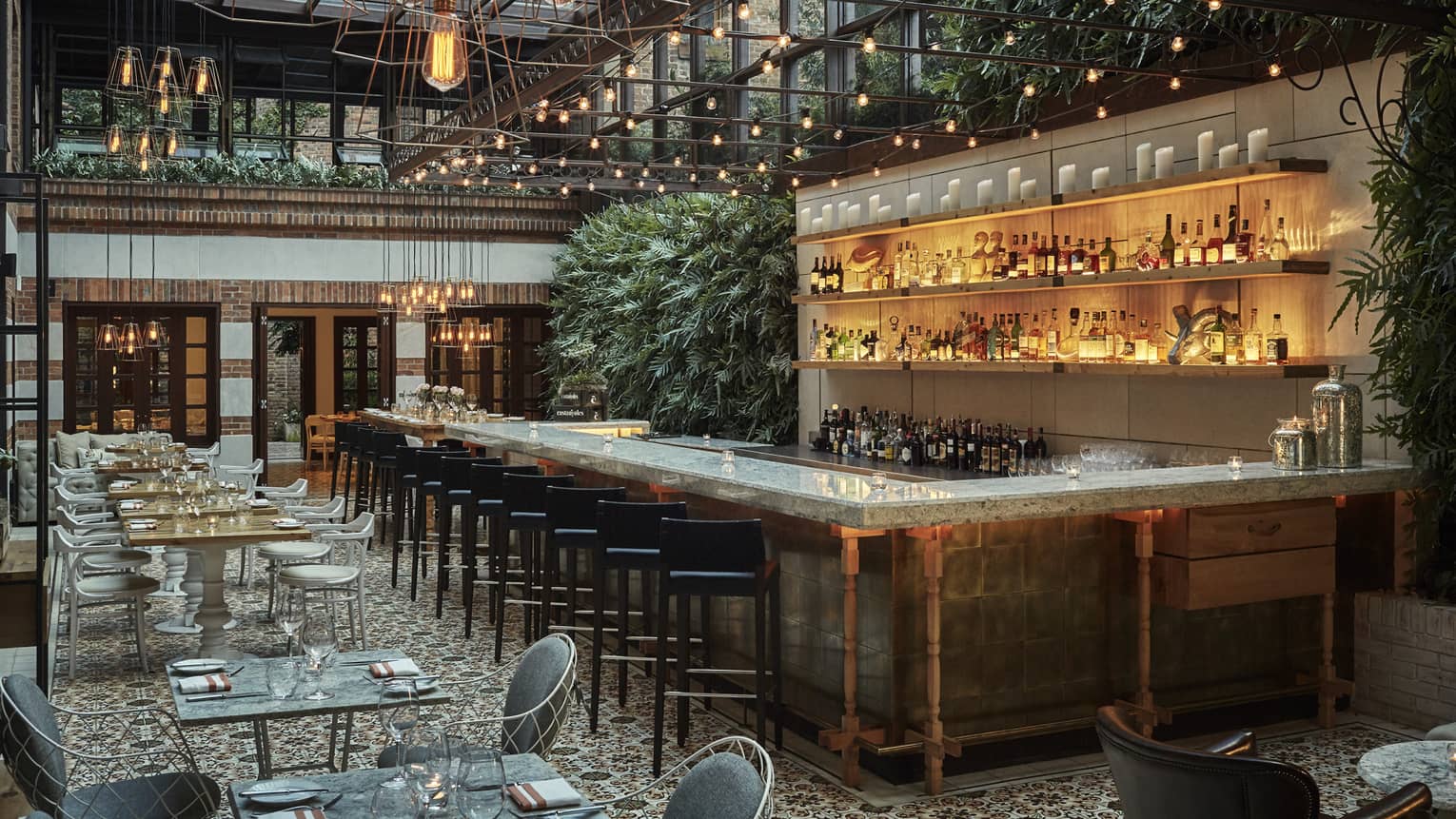 Castanyoles loft-style dining room under skylight and hanging lamps, long illuminated bar, green plants