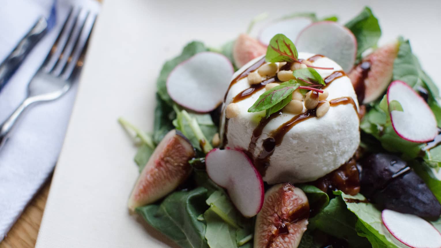 Green salad with fresh figs and radish slices, goat cheese sprinkled with dressing, pine nuts