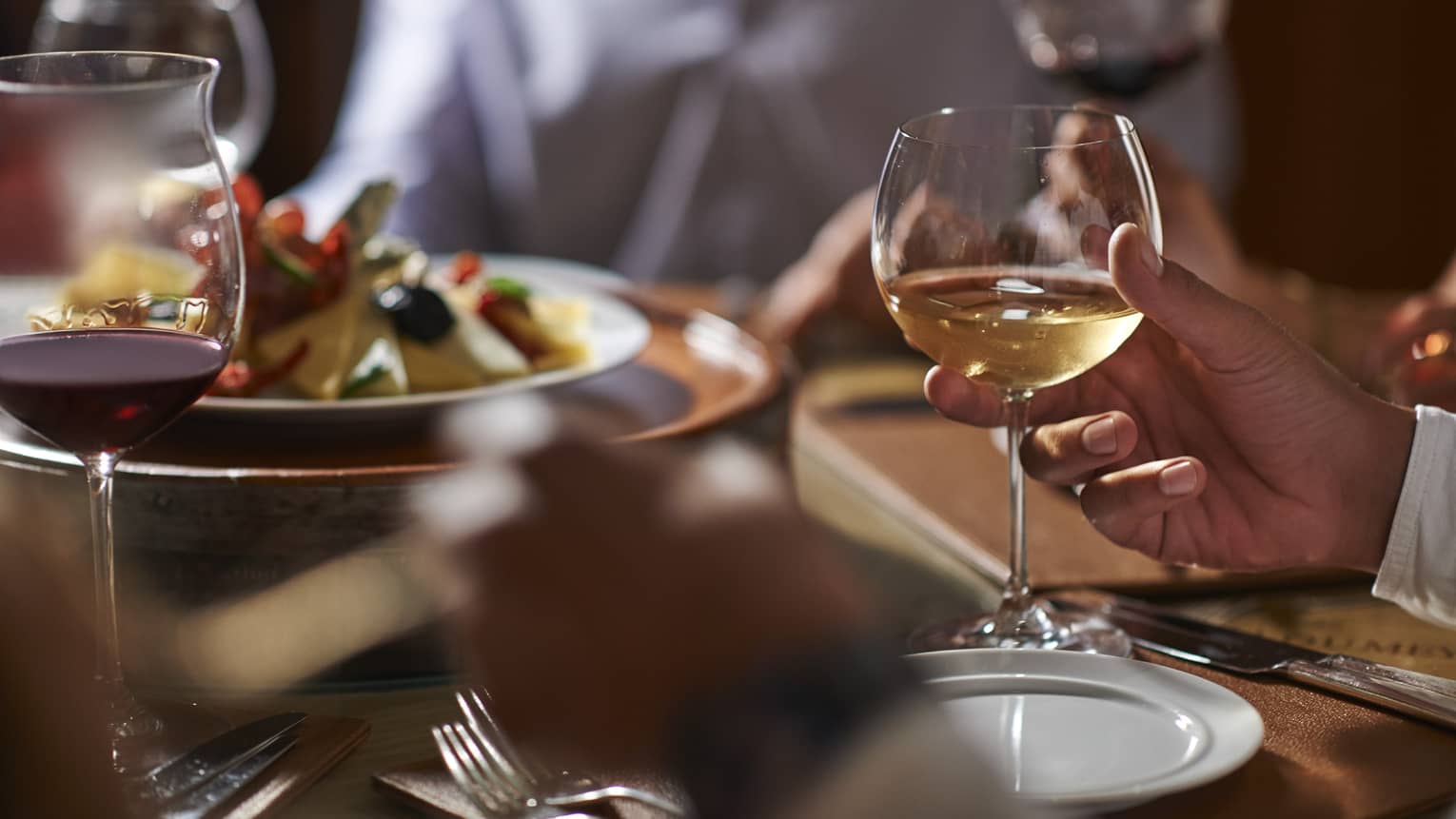 Close-up of man's hand holding a glass of white wine at formal dinner table