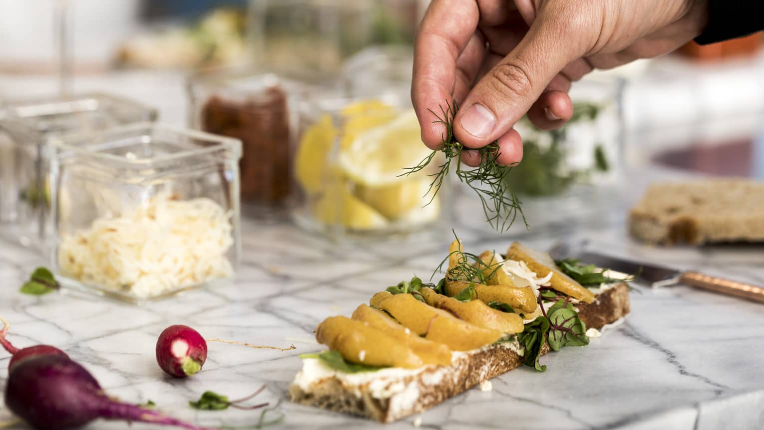 Hand sprinkling fresh herbs on open-faced sandwich on counter