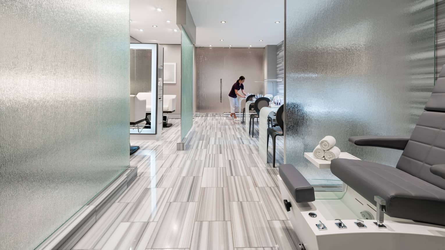 Modern spa with frosted glass walls, pedicure station, staff setting manicure tables
