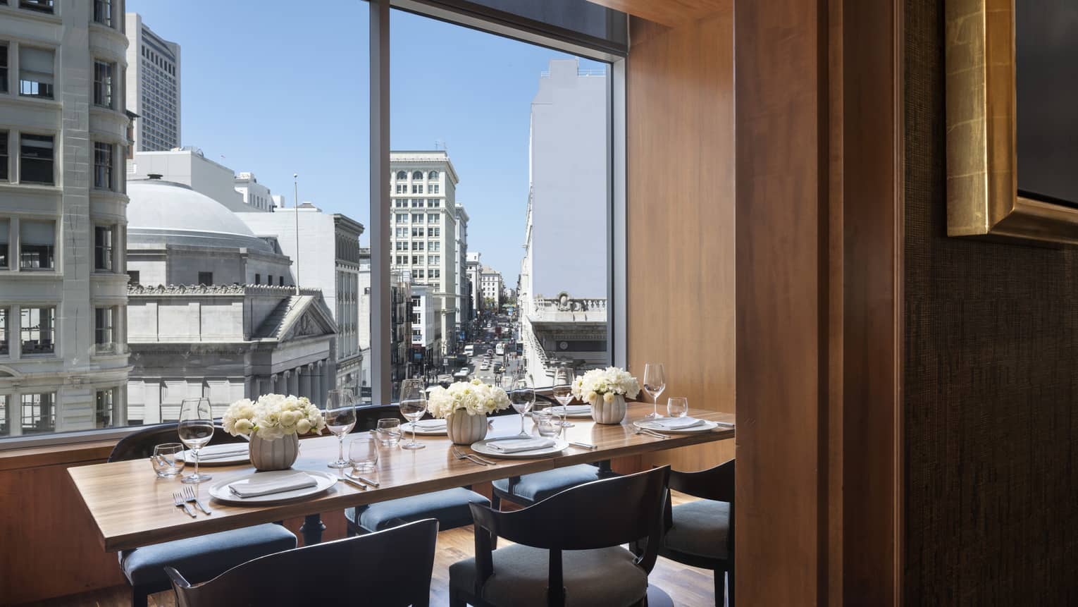 Private dining table set with white flowers under floor-to-ceiling window with sunny city view