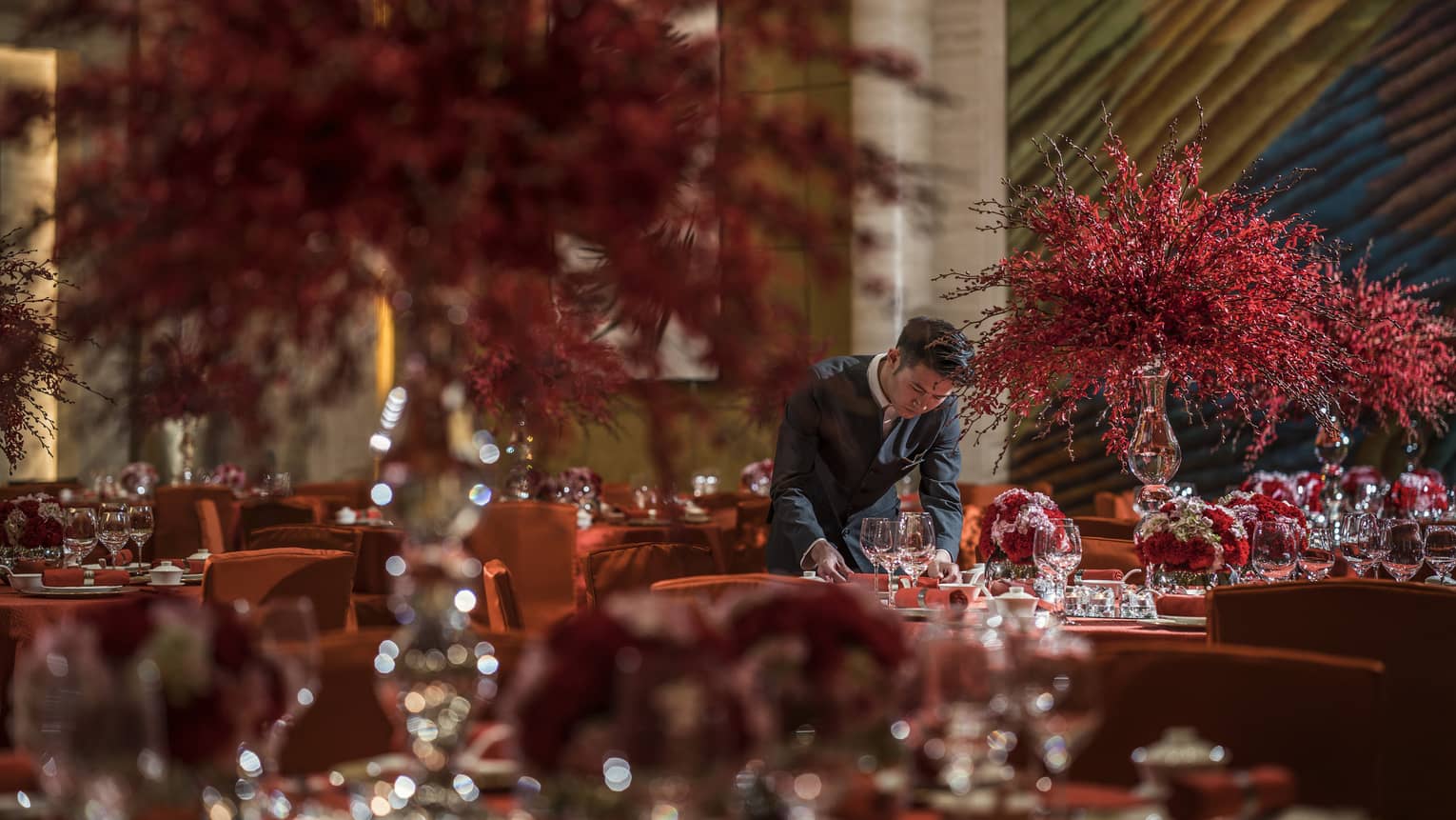 Hotel staff sets banquet tables with large red flower arrangements