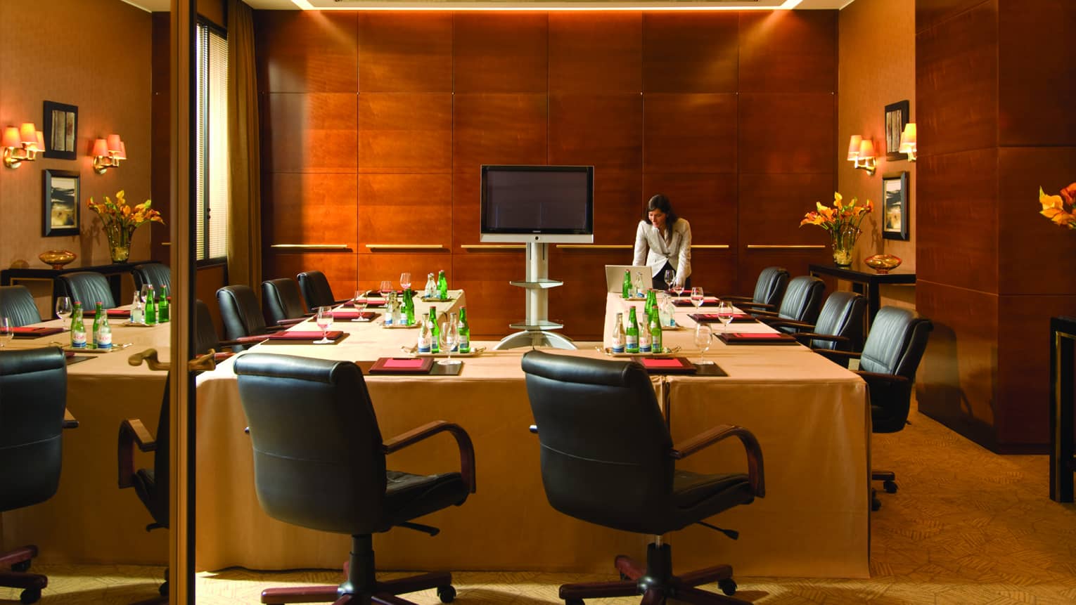 Businesswoman sets up laptop at head of modular meeting table in wood panel room