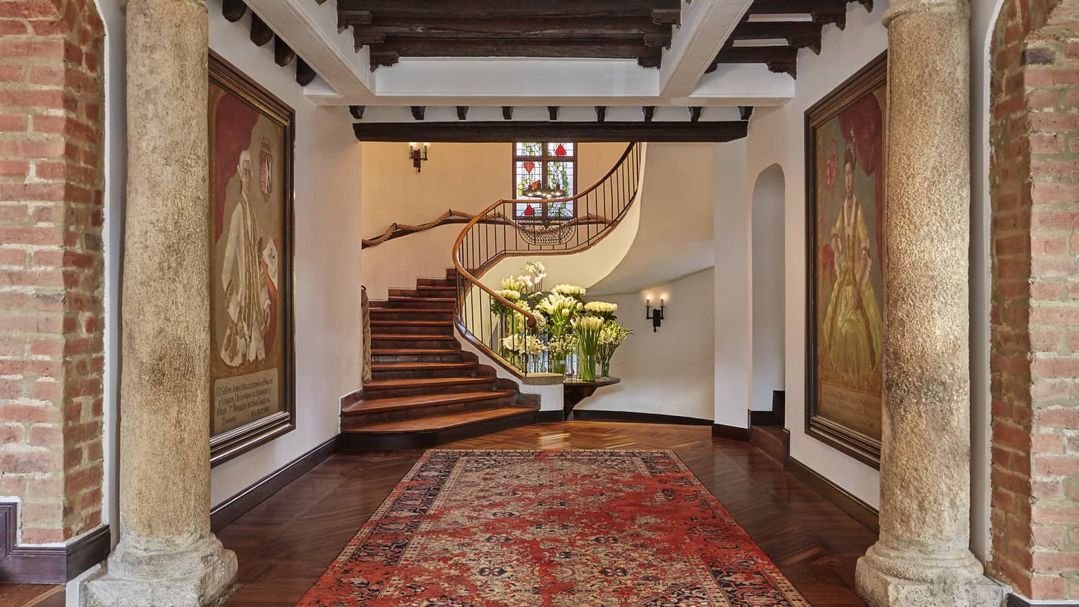 Hotel lobby with stone pillars, carpet and paintings in front of spiral staircase 