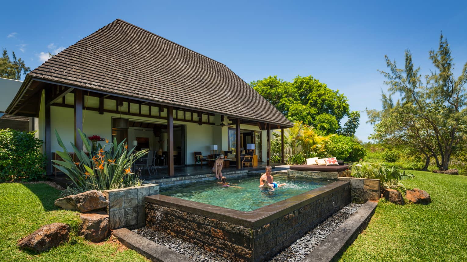 Family swims in private stone pool in front of luxury villa