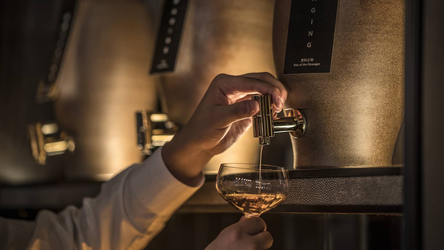 Hand pouring liquor from tap on small modern brass keg with dim lighting