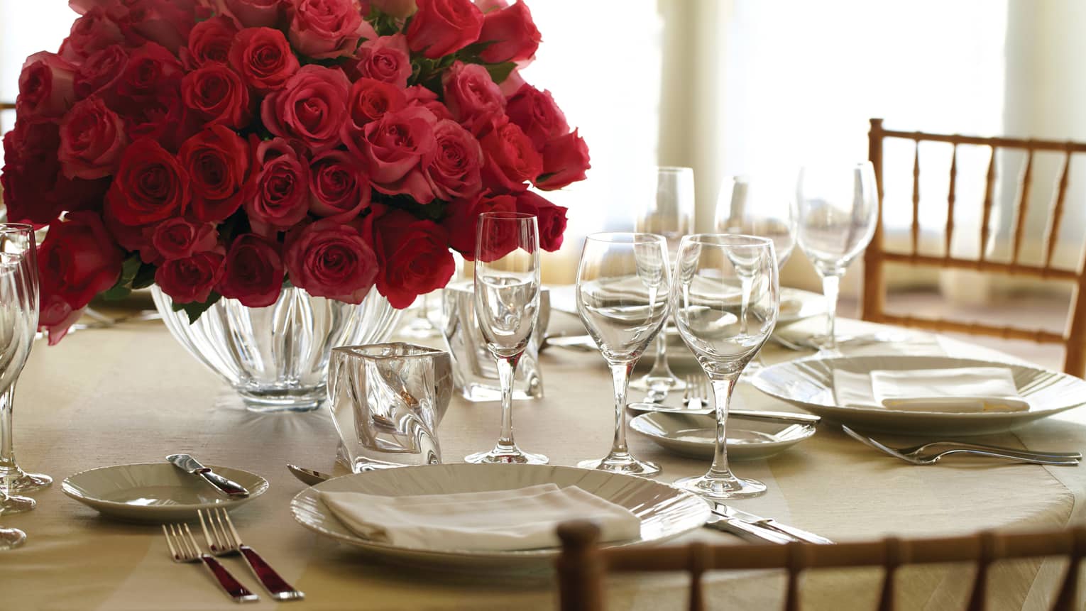 Close-up of round banquet table in Grand Ballroom with wine glass, dishes, vase full of large red rose bouquet