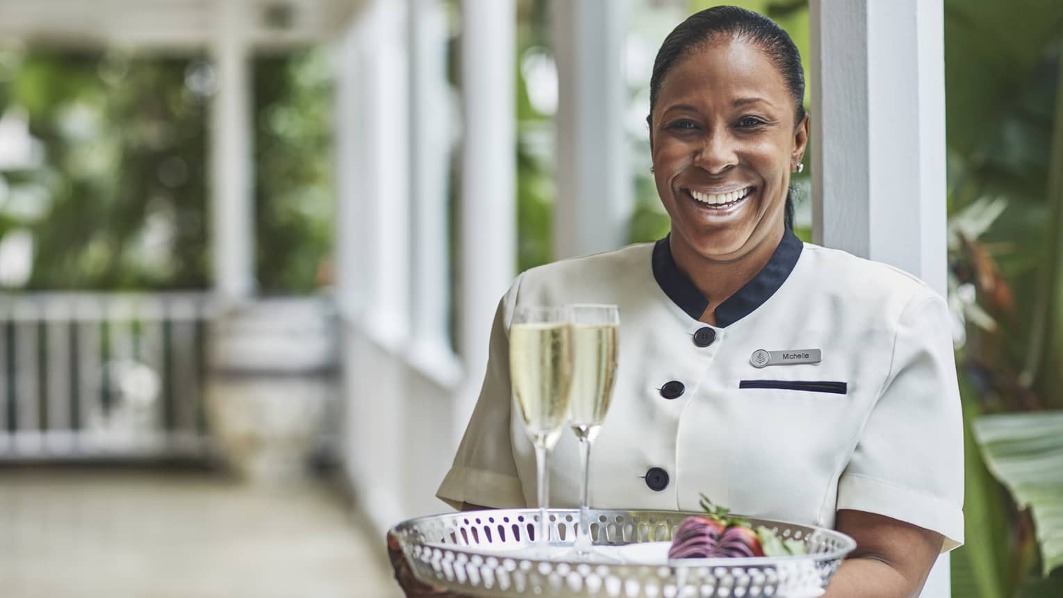 Smiling hotel staff holds tray with two glasses of Champagne