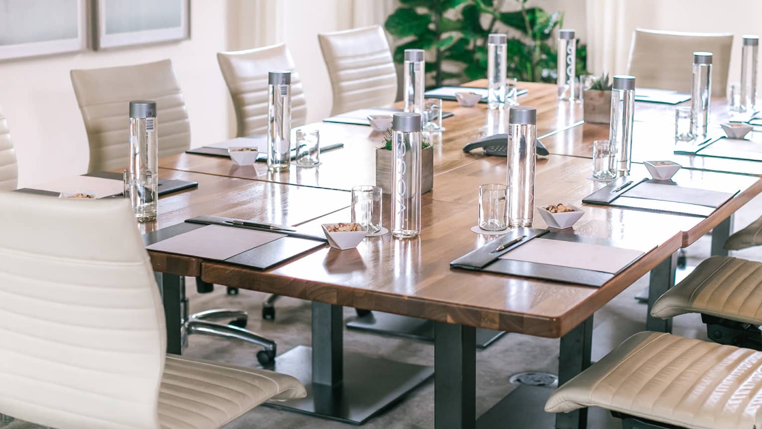 Square meeting table lined with white leather swivel chairs in sunny boardroom