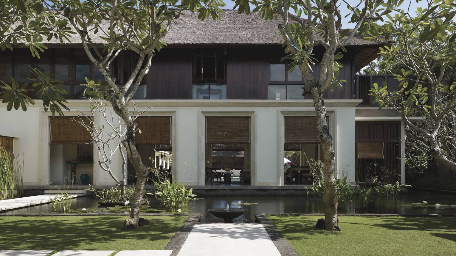 Exterior villa view with pond, small fountain, manicured green lawn, tropical trees