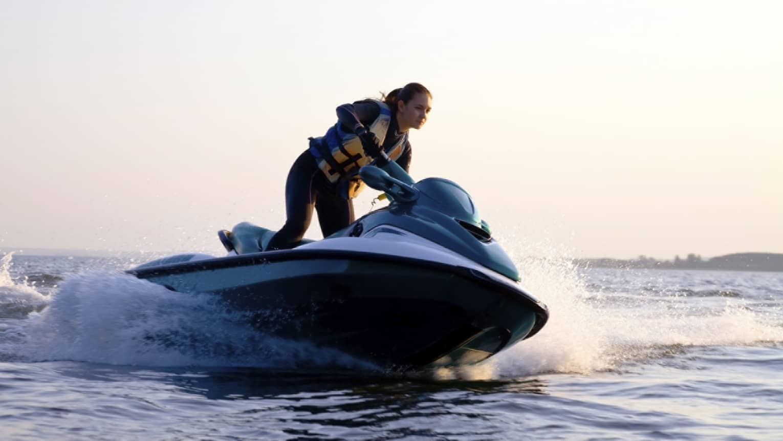 Woman wearing life jacket stands, steers jet ski on ocean at sunset